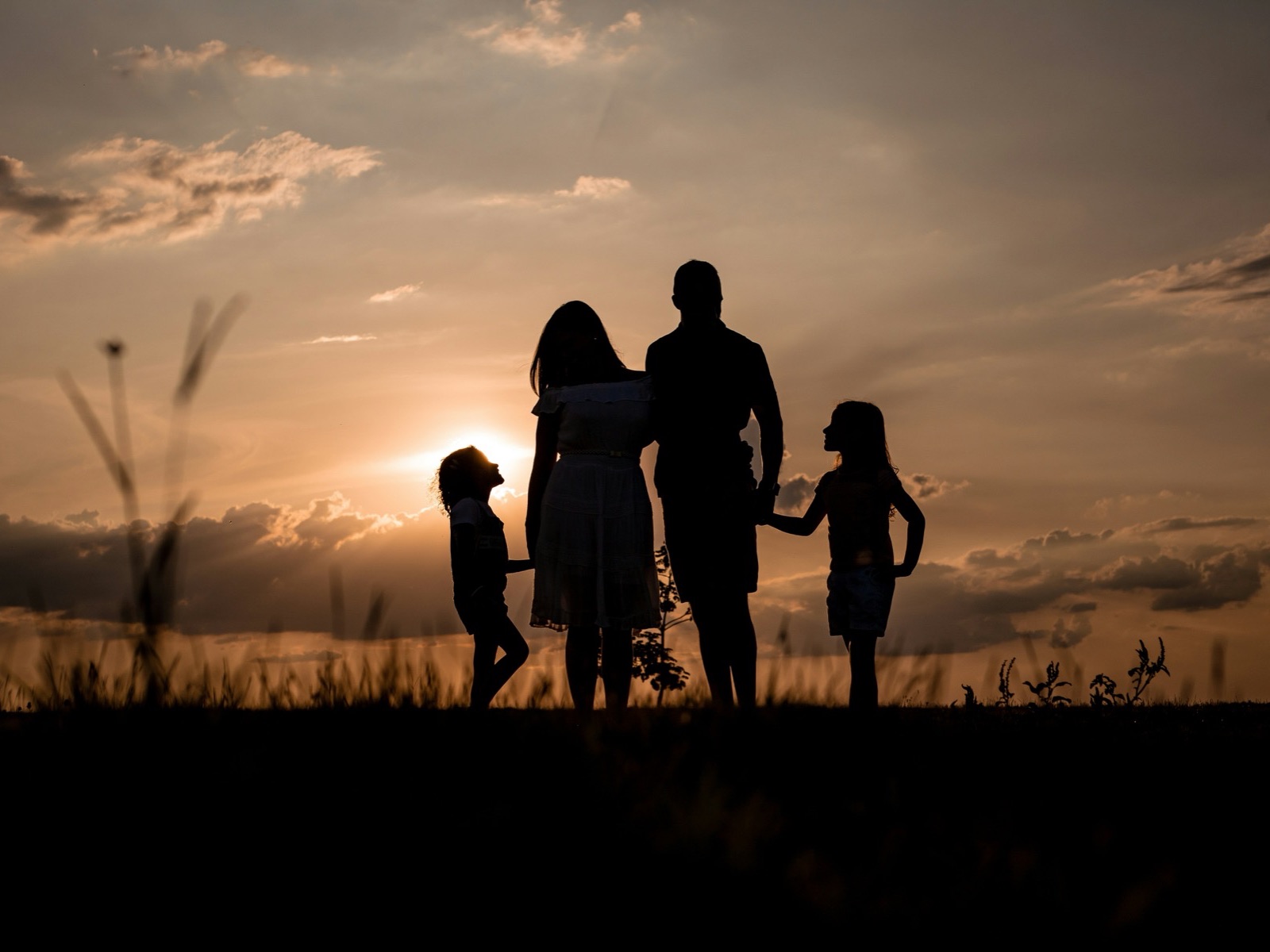 En familie står sammen som silhuetter ved solnedgang